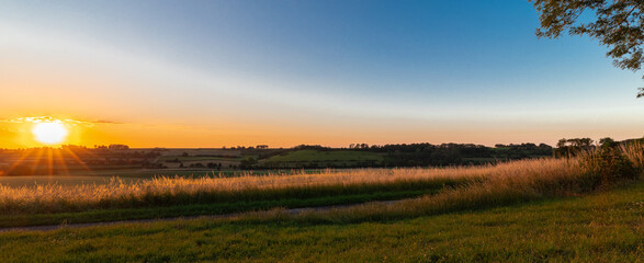 Sunset over the rolling hills in Elkenrade in the of south Limburg in the Netherlands with a spectacular view over the fields, full of wheat and some amazing beams from the sun during golden hour.