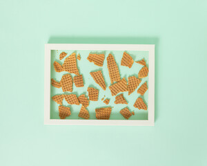 Frame filled with broken ice cream cone on pastel green background. Minimal sweet refreshing summer season concept. Tasty tropical flat lay idea with creative copy space.