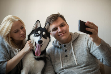 Obraz premium Happy young couple taking a selfie together with dog on the couch at home