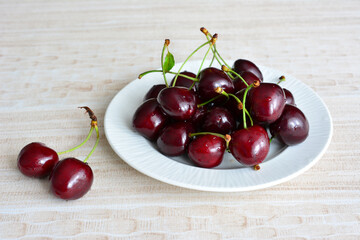 dark red cherries on white plate on beige background, close-up