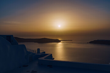 Breath-taking view from Imerovigli in Santorini across the sea. Sunsetting in the distance highlighting the blue sea with yellow and orange tones. - obrazy, fototapety, plakaty