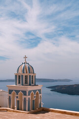 Portrait orientation photo of interesting religious architecture in Santorini, Greece. Seascape and volcano landmass in the background.