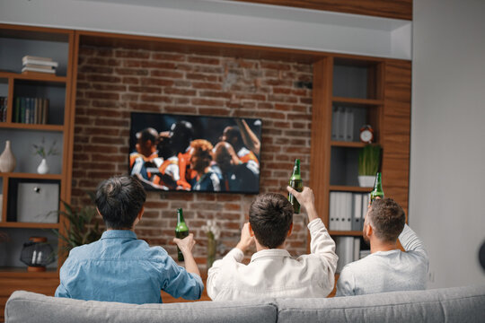 Back View Of Men Watching A Football Game On Tv And Sitting On A Sofa