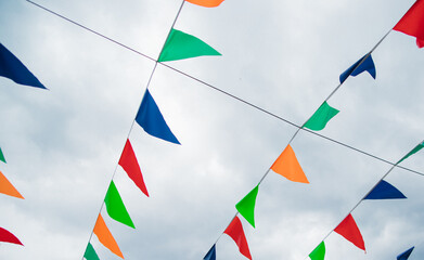 Small, multicolored flags on a blue sky background. Colorful background. Carnival festival, decoration of a park or a street festival.