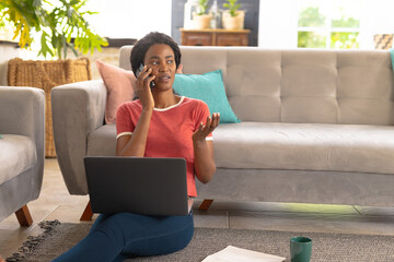 African american young woman speaking on smart phone while freelancing in living room at home