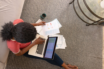 Directly above shot of african american young woman analyzing data while using laptop on carpet
