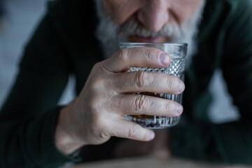 cropped view of senior man drinking whiskey while holding glass.