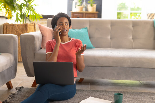African american young woman speaking on smart phone while freelancing in living room at home