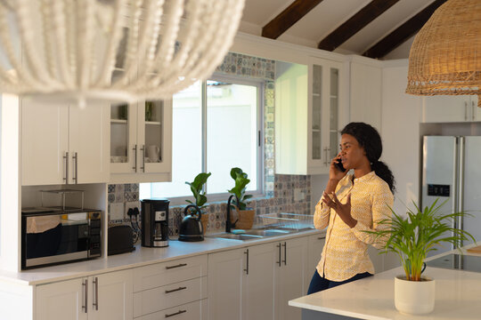 African american young woman gesturing while talking on smart phone in kitchen, copy space