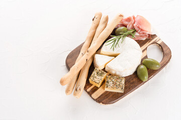 Charcuterie plate at white table - selection of cheeses and meat snacks served with olives and grissini bread sticks. Italian antipasti for aperitif. Restaurant menu background. Copy space