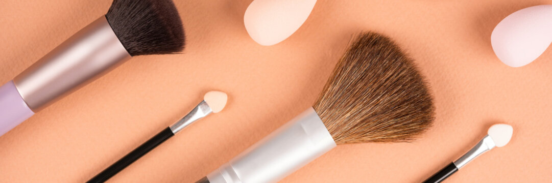 Makeup and beauty concept. Different makeup brushes, sponges and applicators over pastel beige background. Flat lay style banner