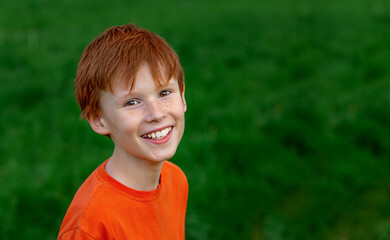 A happy red-haired boy-child smiles, enjoying the adopted life. Portrait of a little boy in nature,...