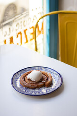 Churros with ice cream in a mexican cafe. Spanish dessert on the white plate with blue ornament on the white table. Yellow metal chair and blue window frame on background