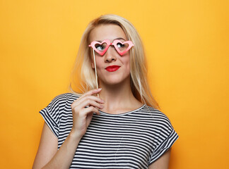 Fototapeta premium Playful young woman holding a party glasses over yellow background.