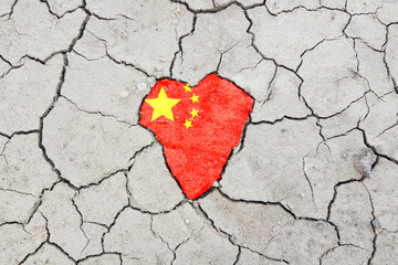 Textured background of cracked dry brown earth with Heart in Chinese Flag Colors