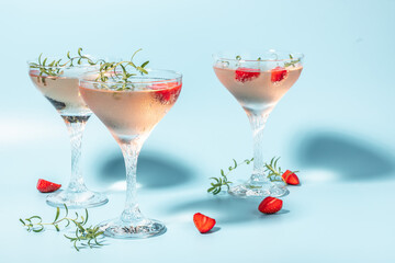 Glass of strawberry cocktail or mocktail, refreshing summer drink with champagne, strawberries, ice cubes and rosemary on blue background
