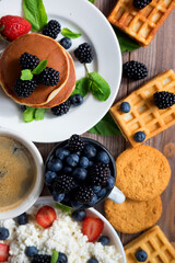 Waffles with blueberries and raspberries on plate. Cottage cheese, Coffee and berries on wooden background. Flat lay.
