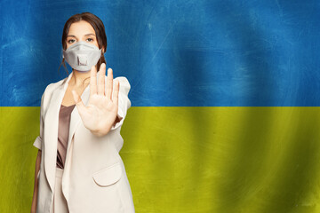 Portrait of serious young woman in protective mask against Ukrainian flag background