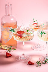 refreshing fruit cocktail or punch with wine champagne, strawberries, ice and rosemary on pink background. Freeze motion splash drops of cocktail