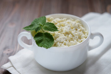 Cottage cheese with mint in a white bowl on a white napkin.