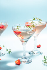 Boozy Refreshing Rose Wine, strawberry cocktail or mocktail, refreshing summer drink with champagne, strawberries, ice cubes and rosemary on blue background