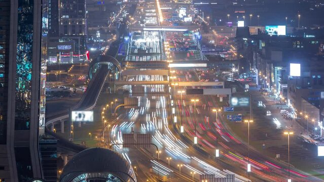 Busy Sheikh Zayed Road aerial night timelapse, metro railway and modern skyscrapers around in luxury Dubai city. Heavy traffic on a highway with many cars. United Arab Emirates