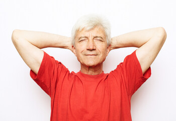 Handsome senior man wearing red t-shirt relaxing and stretching with arms and hands behind head and...