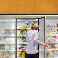 Fototapeta na wymiar Man choosing frozen food from a supermarket freezer... choosing a dairy products at supermarket, reading product information