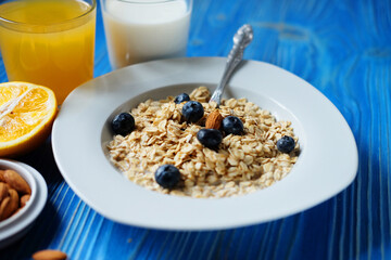 oatmeal with fresh berries on white plate with orange juice and milk, blue wooden background.