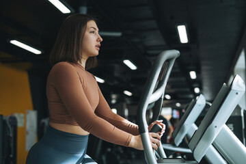 Fototapeta na wymiar Young brunette woman training for cardio equipment at fitness club gym