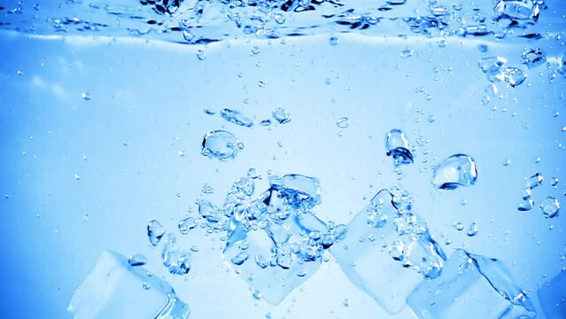 Ice cubes dropped into water with air bubbles.