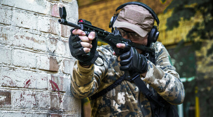 Young man with gun standing sideways near brick wall during advanced firearms, defense tactics, use...