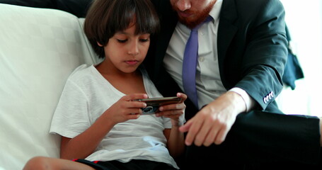 Candid Father and son together at home couch sharing cellphone screen. Mixed race ehtnically diverse parent and child