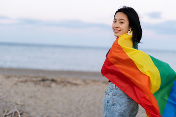 Happy girl with a pride flag at the beach. LGBT community.