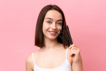 Young Ukrainian woman isolated on pink background holding makeup brush