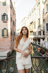Naklejka premium woman in sleeveless jumper looking at camera near fence over venetian canal.