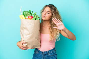 Girl with curly hair holding a grocery shopping bag isolated on green background making stop...