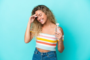 Young blonde woman with a bottle of water isolated on blue background laughing