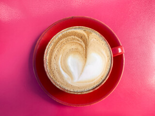 A cup of coffee latte on a red table. Mug of flat white coffee on a red table in red ceramic mug. Coffee art. Heart flower shape latte art. Coffee break, coffee culture. Breakfast.