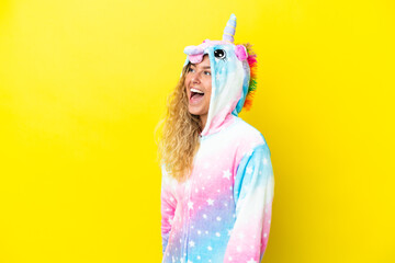 Girl with curly hair wearing a unicorn pajama isolated on yellow background laughing in lateral...