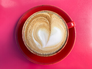 A cup of coffee latte on a red table. Mug of flat white coffee on a red table in red ceramic mug. Coffee art. Heart flower shape latte art. Coffee break, coffee culture. Breakfast.