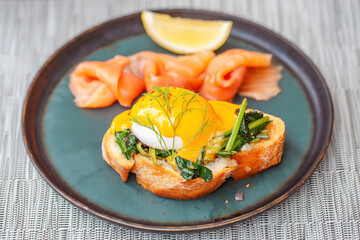 Fresh eggs Benedict with smoked salmon and slice of lemon on plate in restaurant. Gourmet hotel food with baked toast bread and poached egg, healthy snack. Delicious lunch in cafe.