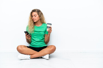 Girl with curly hair sitting on the floor holding coffee to take away and a mobile