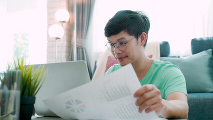  Close-up of a young Asian man wearing a green shirt, explaining his work through a laptop computer, and a piece of paper which is his work, and has a smiling face and gesture.