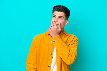 Young handsome caucasian man isolated on blue bakcground having doubts and with confuse face expression