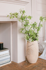 Flowering branches in a vase, bed, fireplace, books. Minimalistic stylish interior.