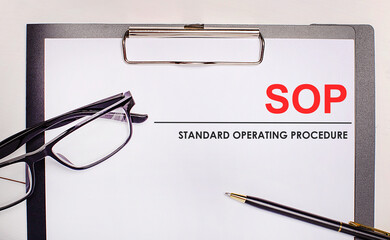 On a light wooden background glasses, a pen and a sheet of paper with the text SOP Standard Operating Procedure. Business concept