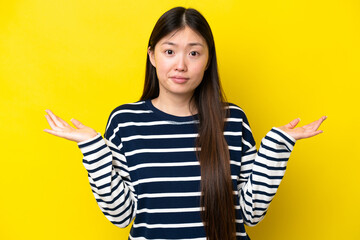 Young Chinese woman isolated on yellow background having doubts while raising hands