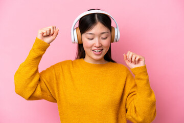 Young Chinese woman isolated on pink background listening music and dancing