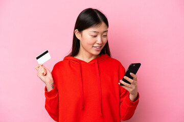 Young Chinese woman isolated on pink background buying with the mobile with a credit card